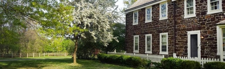 An outside view of the Peachfield house with white fences, a blooming tree, and green grass outside.
