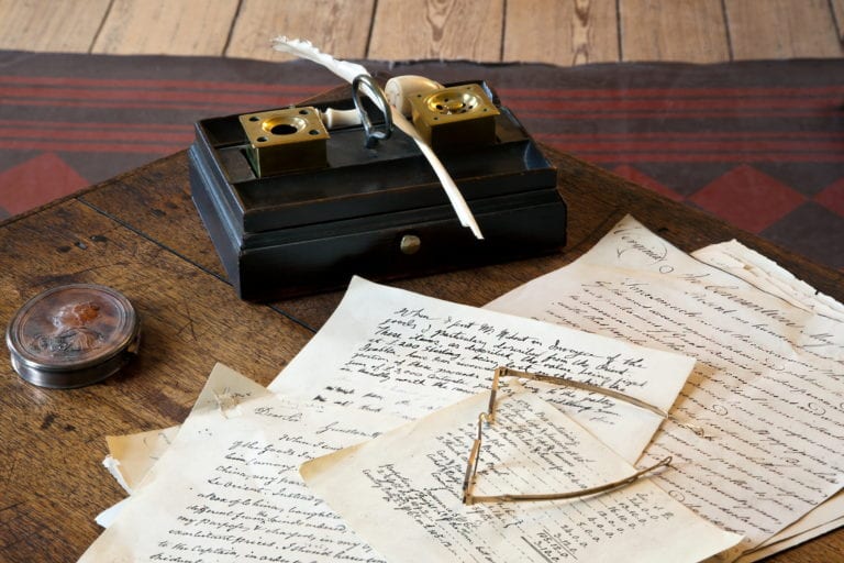 A ink quill, paper, and glasses on a desk inside George Mason